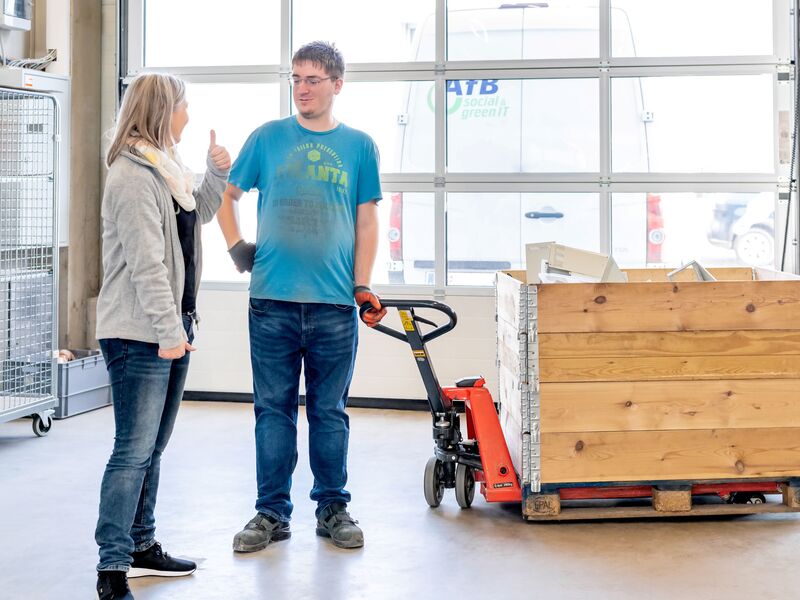 Arbeitskraft mit Assistentin und Hubwagen