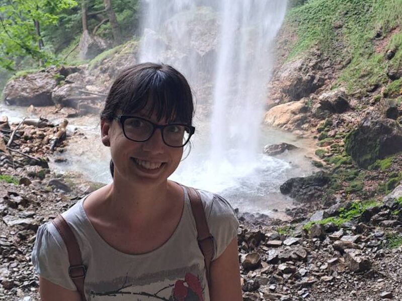 Birgit lächelt und steht vor einem Wasserfall
